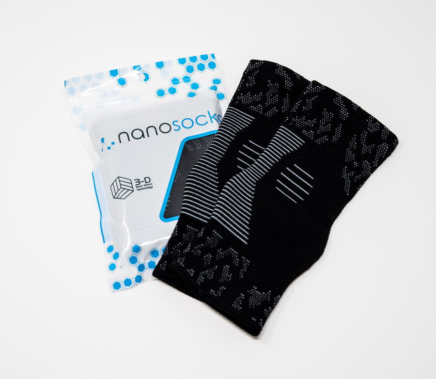 A sealed NanoSocks retail sleeve lying next to a folded pair of the black socks on a white surface.