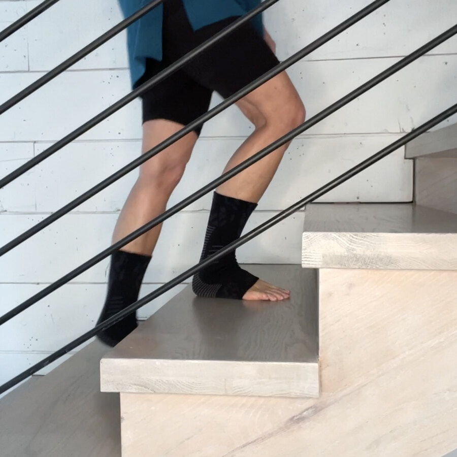 A person walking down a staircase at home in the black socks, the uncovered toes gripping the tread.